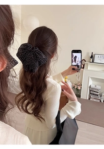 Detailed view of a large black polka dot bow hair clip worn on a low ponytail