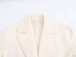 Detail shot of notched lapel and soft wool blend fabric on a light beige long coat