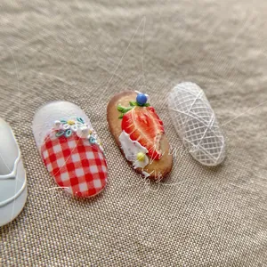 Macro detail of 3D embossed strawberry and plaid lace nail art charms on fabric background