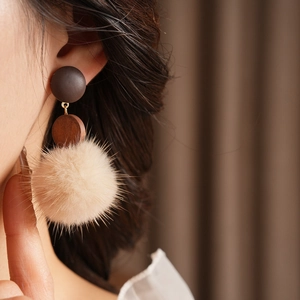 Close-up of a vintage round wooden stud earring with a beige faux fur pom pom detail