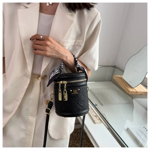 Detail of black embossed barrel bag with gold hardware and decorative silk scarf