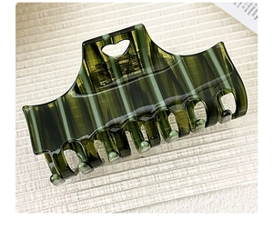 Detail of dark green hair claw clip with vertical stripes and heart-shaped cutout handle