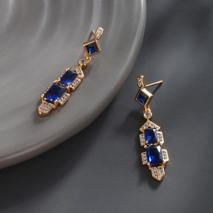 Macro view of gold plated earrings featuring three blue geometric cubic zirconia stones