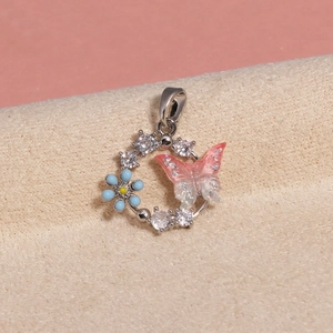 Macro shot of silver ring pendant with pink glitter butterfly and blue enamel flower detail