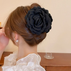 Elegant large black fabric flower hair claw clip worn by a model in warm indoor lighting