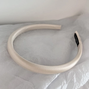 Detailed view of beige satin headband with handmade label on white textured background