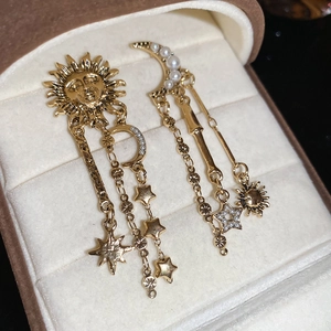 Detail of celestial gold tassel earrings with sun, moon, and pearl charms in jewelry box