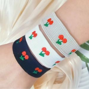 Close-up view of three embroidered cherry wristbands in black, white, and grey fabrics