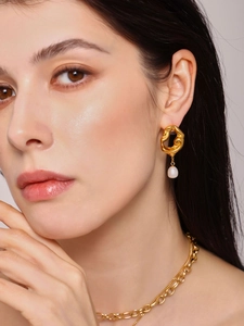 Détail d'une boucle d'oreille dorée à texture lave avec perle d'eau douce sur un modèle
