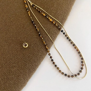 Macro shot of double-layer tiger eye bead necklace with gold chain on brown felt