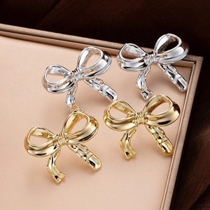 Close-up of gold and silver metallic bow earrings on a beige velvet jewelry tray