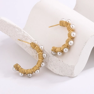 Detailed close-up of C-shaped gold hoop earrings with vertical texture and white pearls