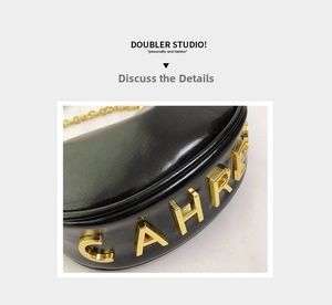 Detailed view of black leather crescent bag with 3D gold metal lettering and chain strap