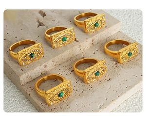 Macro shot of gold evil eye rings with green stones on a grey stone background