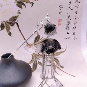 Macro shot of silver Chinese fan hairpin with black rose and ink wash tassels on scroll
