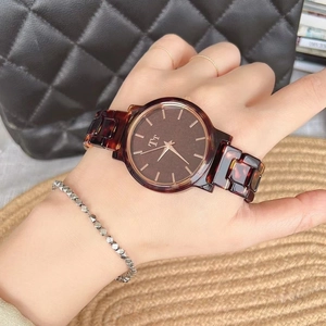 Detail of a brown tortoiseshell patterned women's watch with gold hands on a leather strap