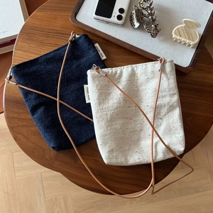 Detail view of denim and beige embroidered fabric crossbody bags with slim cord straps