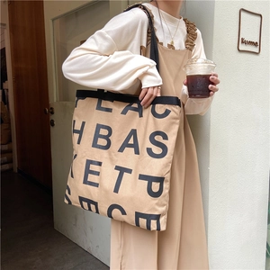 Detail of a large beige canvas tote bag with black lettering shown in a street setting