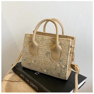 Detailed embroidery of flowers on beige straw woven tote bag with leather straps