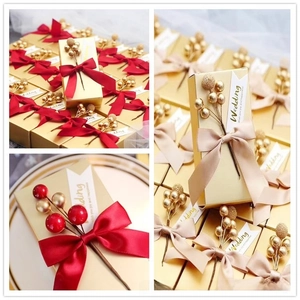 Detailed view of wedding favor gift box with gold ribbon and red artificial berries decoration