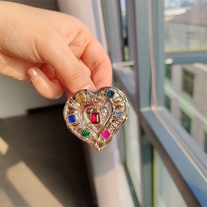 Vintage gold heart brooch with colorful crystals held against a soft outdoor background