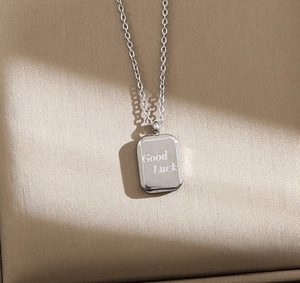 Macro shot of silver rectangular pendant with Good Luck engraving on fine link chain