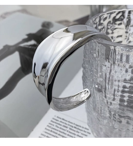 Detail of wide open cuff bracelet with polished silver finish on glass texture background