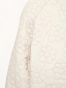 Detailed close-up of cream quilted jacket featuring unique floral stitching and glossy texture