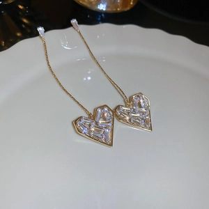 Dettaglio macro di orecchini lunghi in oro con cuori in zircone su piatto ceramica