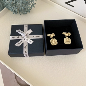 Detailed shot of beige square stud earrings with golden H logo and gift box
