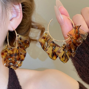 Detail of leopard print petal C-shaped earrings worn by a model in warm lighting