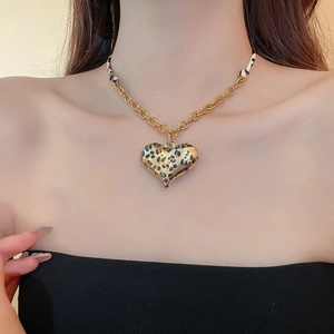 Detail of leopard print heart pendant on gold chain necklace worn by a model