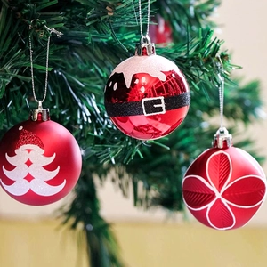 Trois boules de Noël rouges avec motifs de Père Noël suspendues sur un sapin de Noël vert
