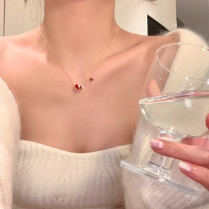 Detail of gold-plated necklace with red enamel puppy and heart pendants on white knitwear
