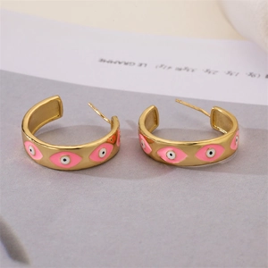Detailed macro view of gold-plated C-shaped earrings with pink enamel and evil eye motif