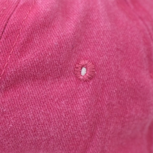 Macro shot of embroidered ventilation eyelet on washed pink cotton baseball cap fabric