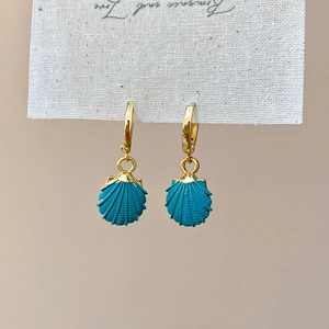 Detailed close-up of golden hoop earrings with blue shell pendants on white packaging