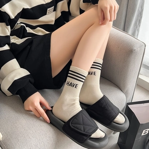 Détail de chaussettes blanches avec broderie « HAVE » et sandales matelassées noires