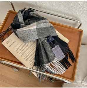 Close-up of grey and black plaid cashmere-feel scarf with fringe on a wooden tray