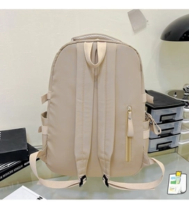 Detail view of the breathable mesh handles and anti-theft back pocket on the beige backpack