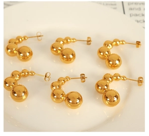 Macro detail of gold pea pod stud earrings with polished gradient spheres on white plate