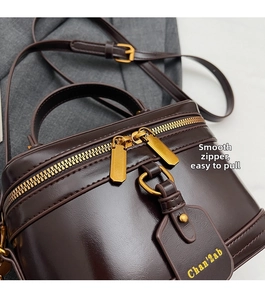 Detailed close-up of dark brown leather box bag featuring a smooth gold dual zipper closure