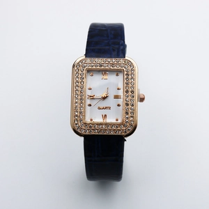 Macro detail of square rose gold watch case with crystal bezel and blue leather strap