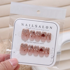 Detail of pink gradient press-on nails featuring glitter, dots and red heart patterns
