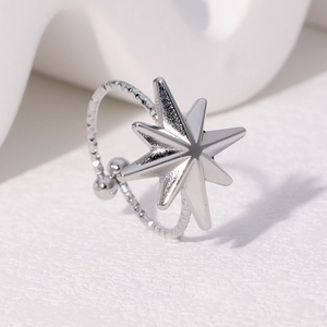 Minimalist silver stainless steel eight-pointed star ring with textured band on white surface