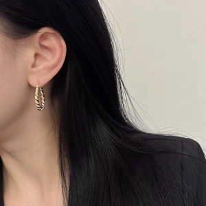 Detailed close-up of a model wearing a gold twisted rope hoop earring with polished finish