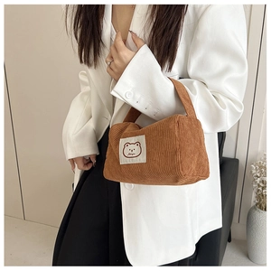 Detail of a brown corduroy handbag with a cute bear patch held by a woman in a white blazer