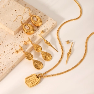 Gold textured earrings and rectangular swirl pendant necklace set on stone blocks