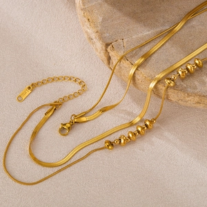 Detail of layered gold stainless steel snake and bead chains on a natural stone background