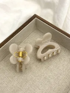 Détail de deux pinces à cheveux papillon beige sur un plateau en bois avec ressort doré